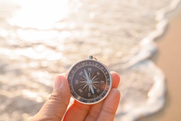 Close up hand holding compass with beach background