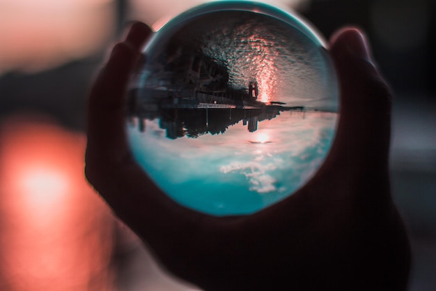 Foto close-up di una mano che tiene una palla di cristallo contro il lago al tramonto