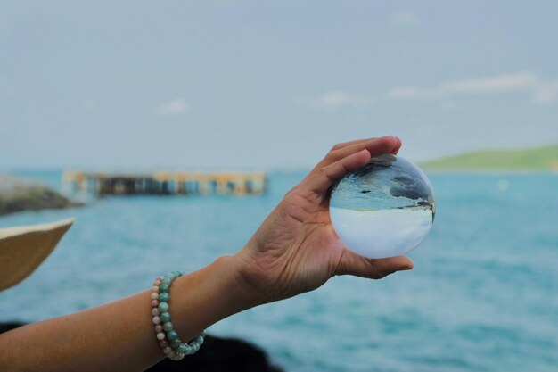 Foto close-up di una mano che tiene una palla di cristallo contro il mare