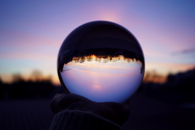 Foto close-up di una mano che tiene una palla di cristallo contro il cielo durante il tramonto