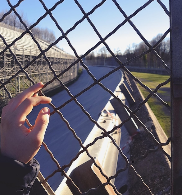 Foto close-up di un cane che tiene la mano contro una recinzione a catena