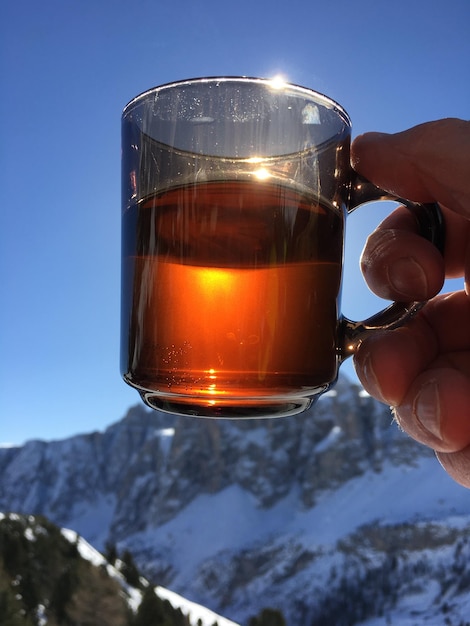 Foto close-up della mano che tiene la bevanda contro un cielo limpido