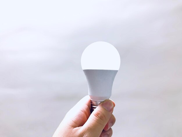 Close-up of hand holding electric bulb against sky