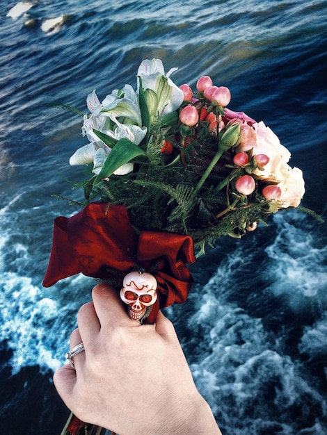 Foto close-up di una mano che tiene un bouquet di fiori sopra il mare