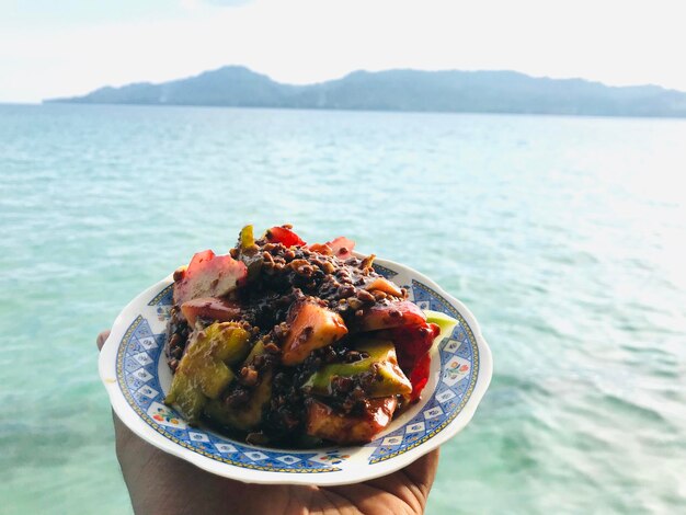 Photo close-up of hand holding food in sea against sky