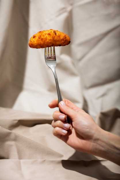 Close up hand holding fork with food croquette