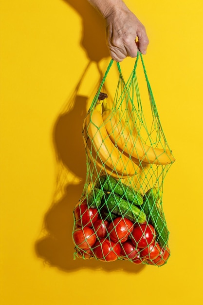 Foto close-up di una mano che tiene la frutta contro uno sfondo giallo