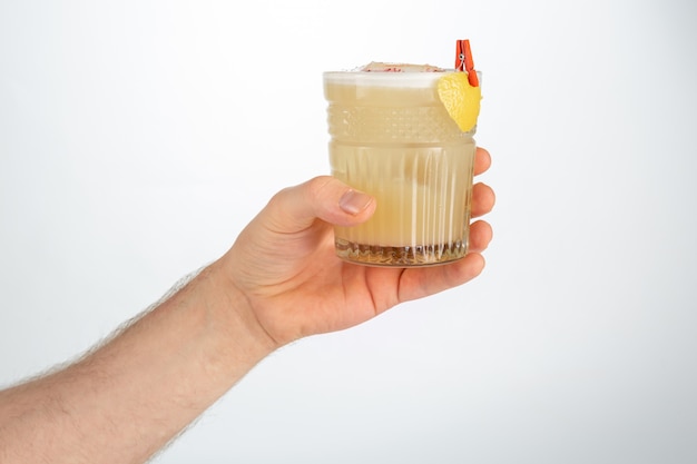 Photo close up of a hand holding a glass of whiskey sour cocktail on white  with copy space.