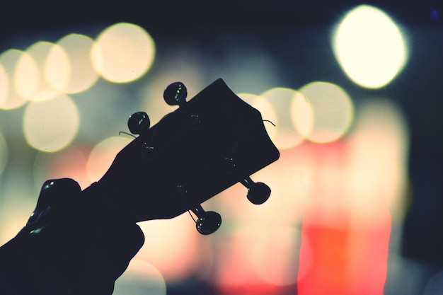 Close-up of hand holding guitar against illuminated background