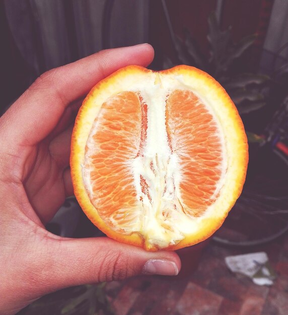 Foto close-up di una mano che tiene un arancione a metà