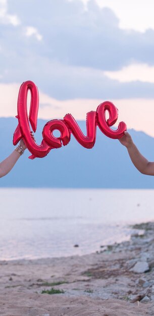 Close-up of hand holding heart shape over sea against sky