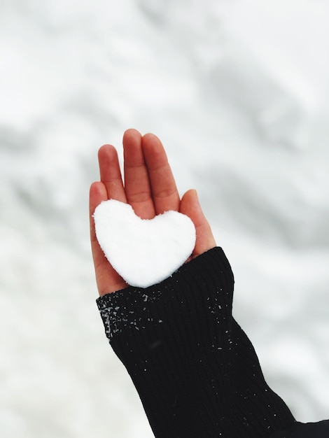 Foto close-up di una mano che tiene la neve in forma di cuore all'aperto