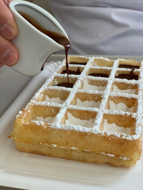 ワッフルの上にホットチョコレートソースを握っている手のクローズアップ