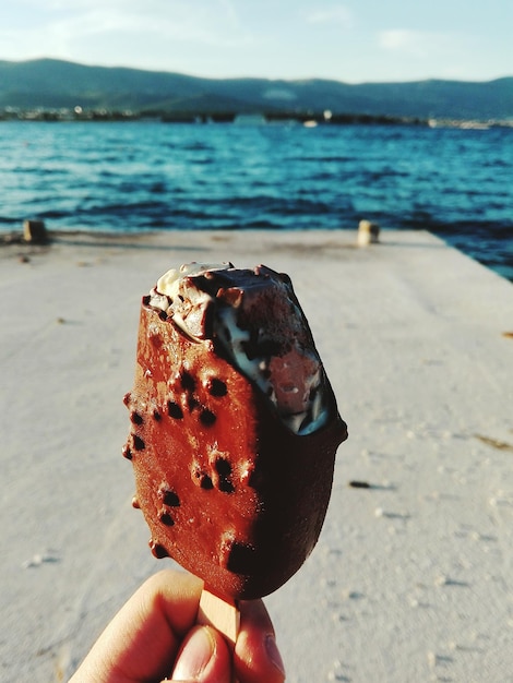 Foto close-up di una mano che tiene il gelato in spiaggia