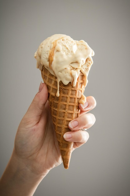 Foto close-up di una mano che tiene un cono di gelato su uno sfondo grigio