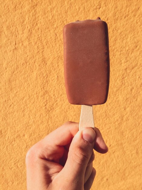 Close-up of hand holding ice cream cone against wall