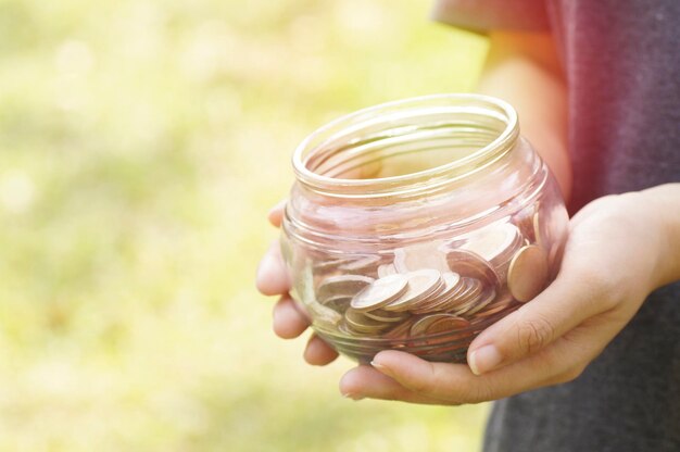 Photo close-up of hand holding jar with coins