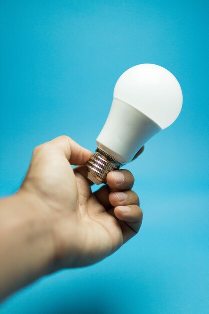 Close-up of hand holding light bulb against blue background