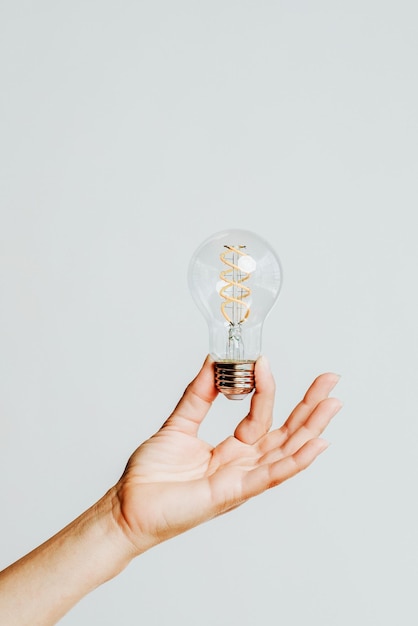 close-up of hand holding light bulb against white background