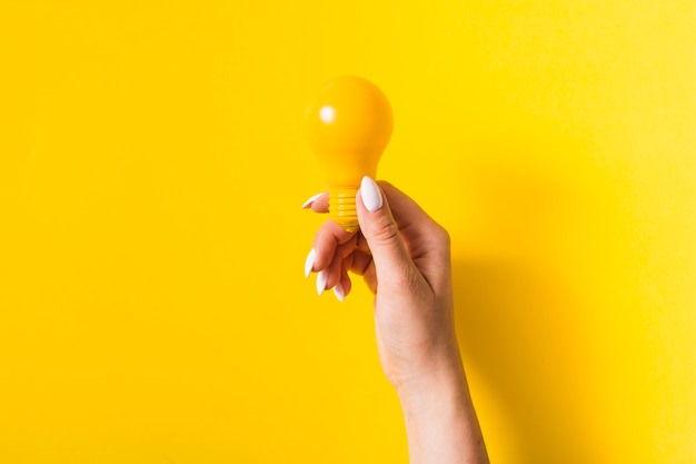 Foto primo piano della mano che tiene la lampadina su sfondo giallo