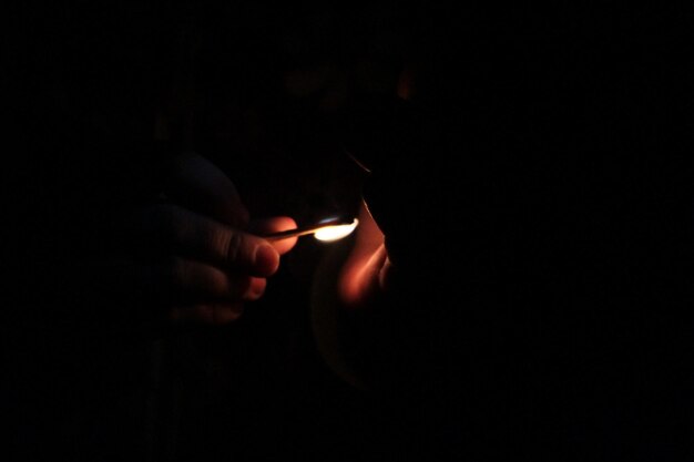 Close-up of hand holding lit candle in the dark