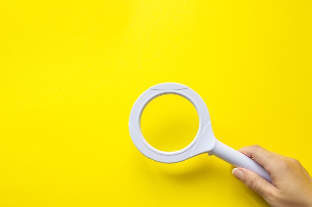 Close up hand holding magnifying glass on yellow background. SEO managment.