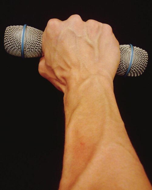 Photo close-up of hand holding microphone against black background