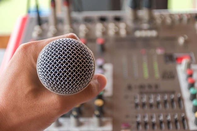 Foto close-up di mano che tiene il microfono sopra il mixer del suono