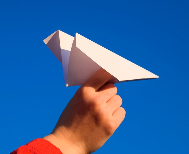 Foto close-up di una mano che tiene la carta contro il cielo blu