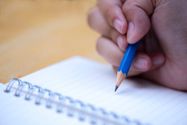  Close up  hand holding pen writing notebook on wood background