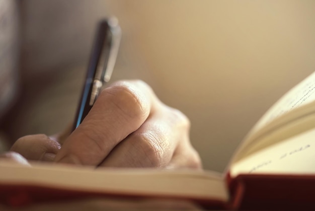 ペンを握って本に書いている手のクローズアップ