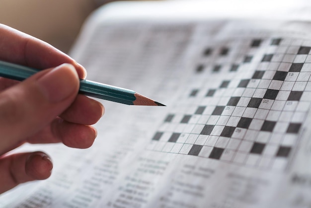 Close up hand holding pencil over crossword puzzle on newspaper