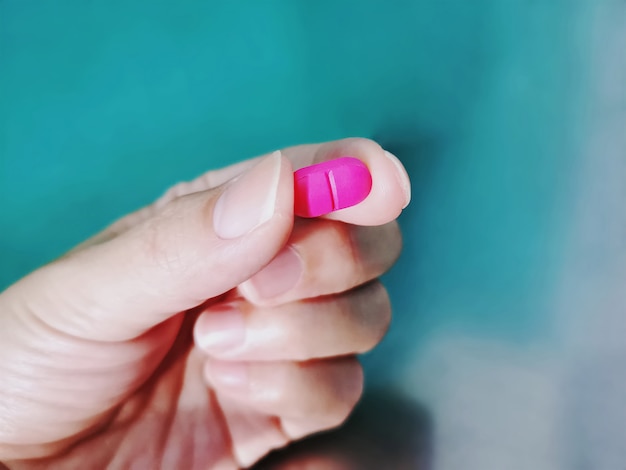 Photo close-up hand holding pink medication pill with selective focus