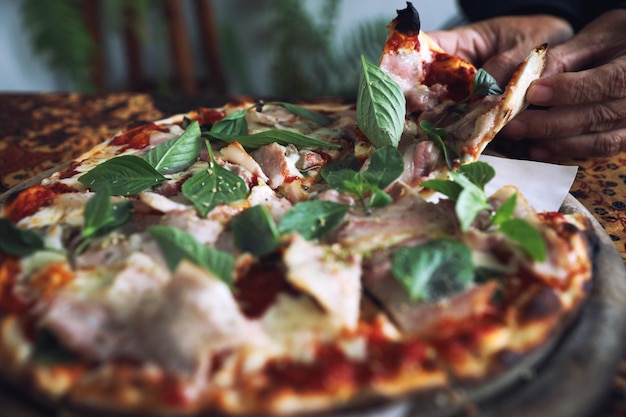 Foto close-up di una mano che tiene la pizza sul tavolo