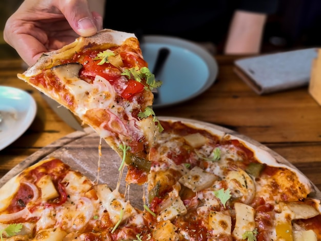 Foto close-up di una mano che tiene la pizza sul tavolo