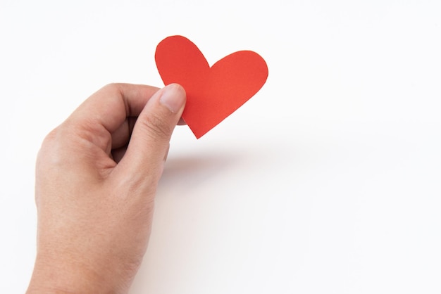 Foto close-up di una mano che tiene carta a forma di cuore rossa su uno sfondo bianco