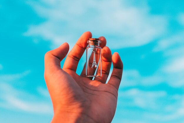 Close-up of hand holding replica eiffel tower in bottle against sky