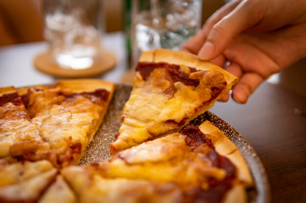 Close-up della mano che tiene una fetta di pizza deliziosa e calda sul tavolo