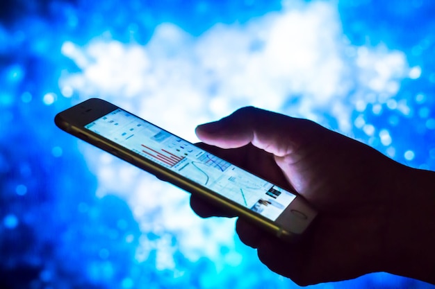 Close-up of hand holding smart phone against blue sky