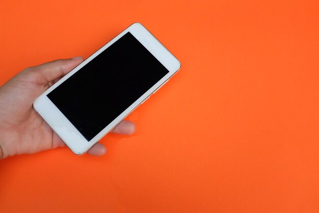 Close-up of hand holding smart phone against orange background