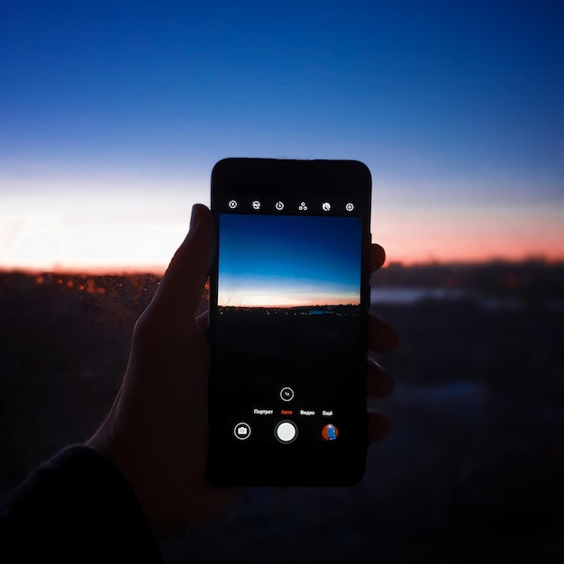 Close-up of hand holding smart phone against sky