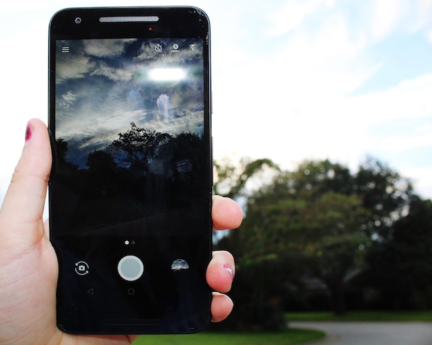 Close-up of hand holding smart phone against sky