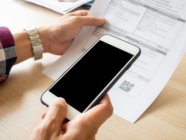 Chiuda sullo smart phone della tenuta della mano per scansionare il codice di qr dalla fattura sui documenti.