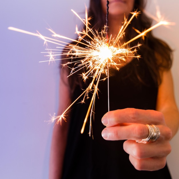 Close-up of hand holding sparkler against sky