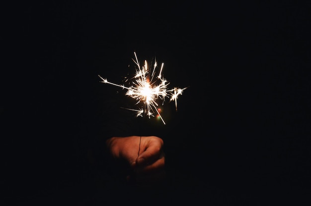 Photo close-up of hand holding sparklers at night