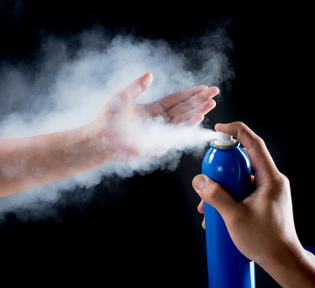 Photo close-up of hand holding spraying over black background