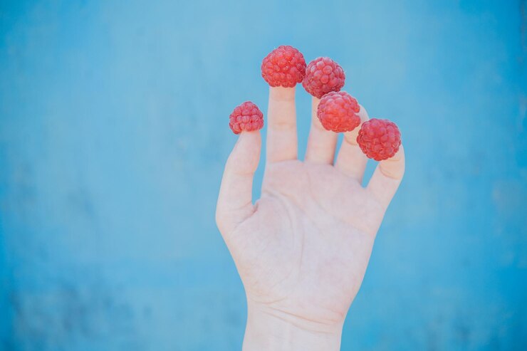 Photo close-up of hand holding strawberry against blue sky