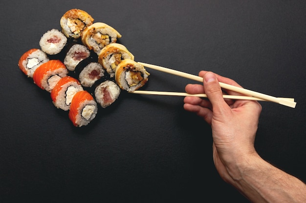 Close up on hand holding sushi roll with chopsticks