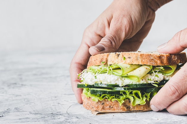 Close-up of a hand holding a vegetarian sandwich with green vegetables. Lettuce, zucchini, alfalfa and cucumber. Vegan food