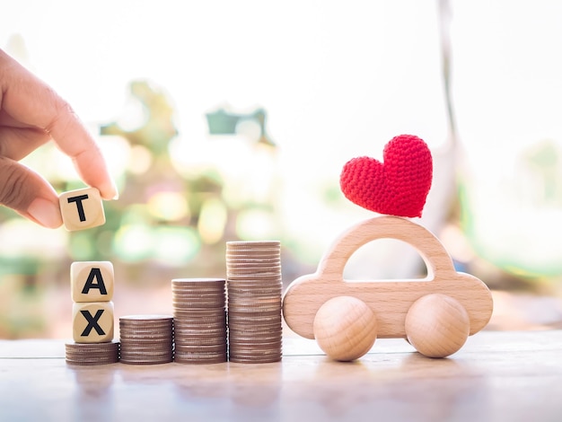 Close up hand holding wooden block with word TAX wooden toy car stack of coins The concept of paying tax for car Car taxes